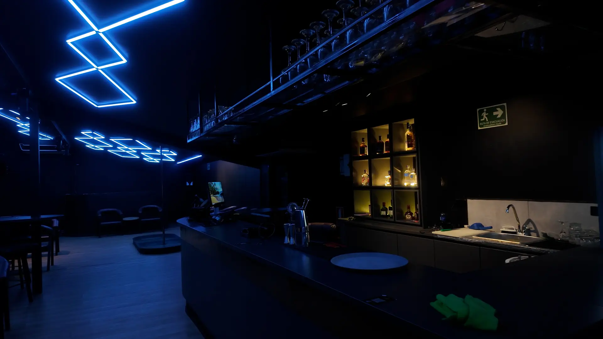 The bar at Club Fase II with lit shelves of spirits and neon lights on the ceiling, Medellín